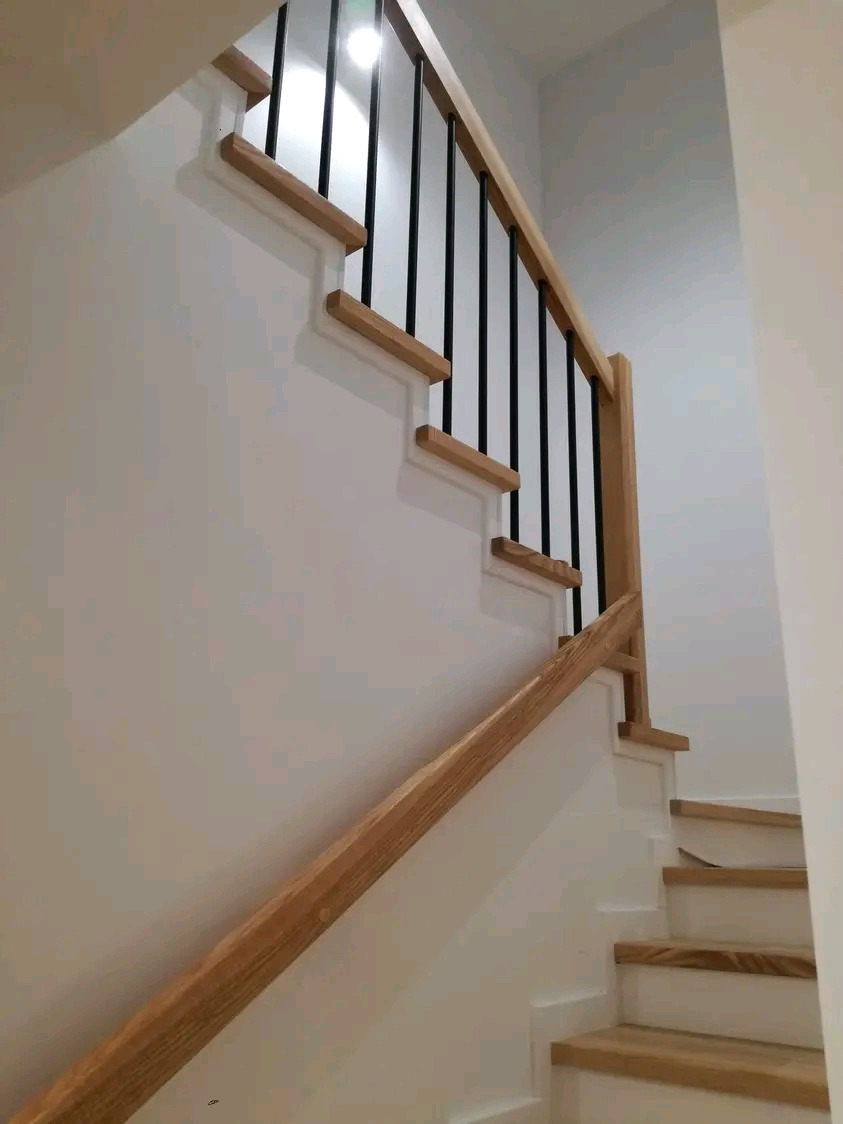 Schody drewniane z jasnego drewna z czarnymi metalowymi prętami balustrady, widok z dołu, minimalistyczny design.