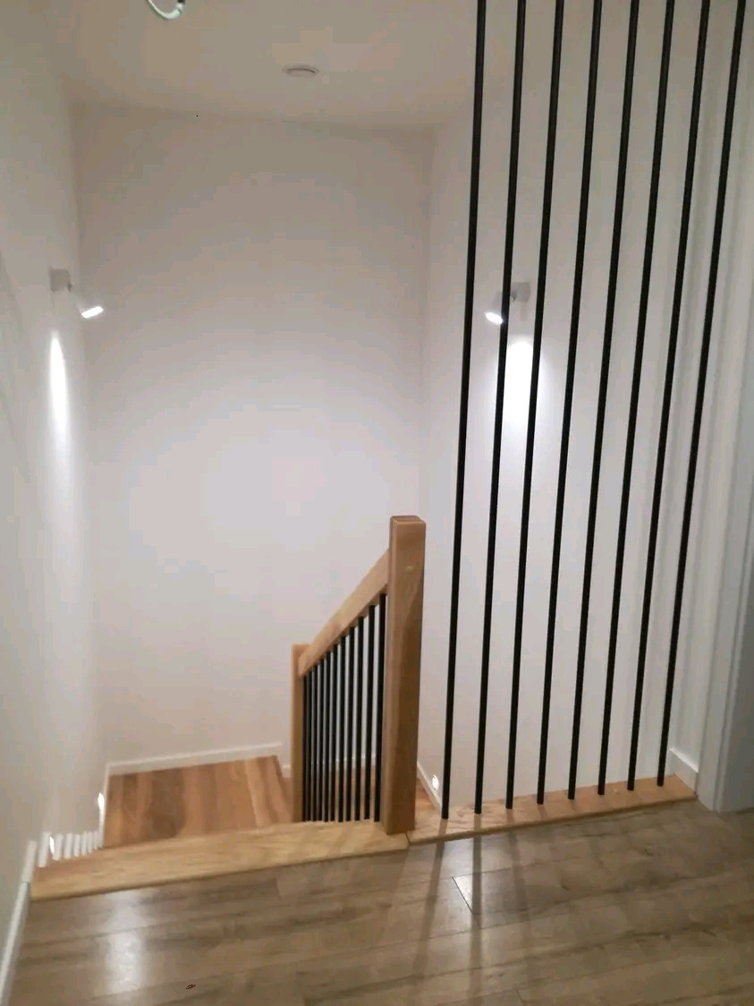 Klatka schodowa z drewnianymi stopniami i nowoczesną balustradą z pionowych, czarnych prętów, widok z góry.