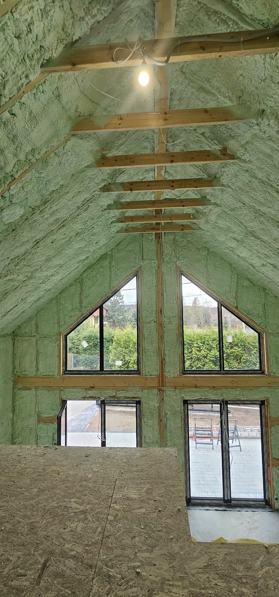 Poddasze ocieplone pianką PUR w Nowym Sączu. Widoczne drewniane belki konstrukcyjne, okna trójkątne i dolne okna przesuwne. Izolacja natryskowa o jednolitej strukturze.