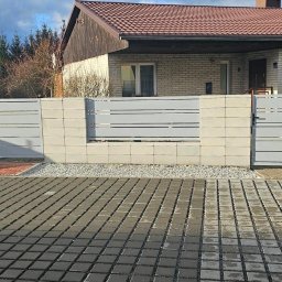 Krzysztof jarosz - Nowoczesne ogrodzenie panelowe z bramą wjazdową, szare panele poziome, betonowe słupki, kostka brukowa na podjeździe, dom jednorodzinny w tle.