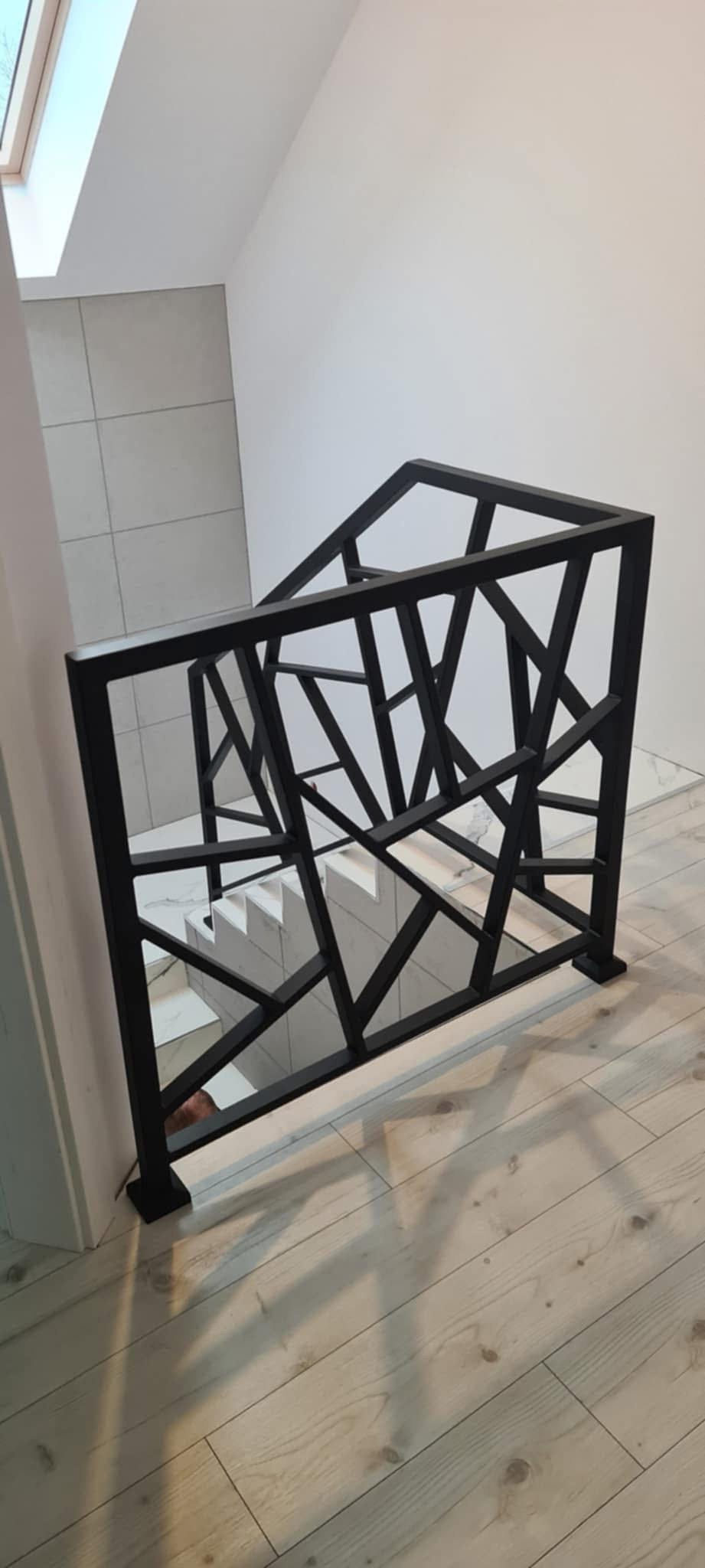 Nowoczesna balustrada schodowa w kolorze czarnym o geometrycznym wzorze, zamontowana w jasnym wnętrzu z drewnianą podłogą i białymi schodami.