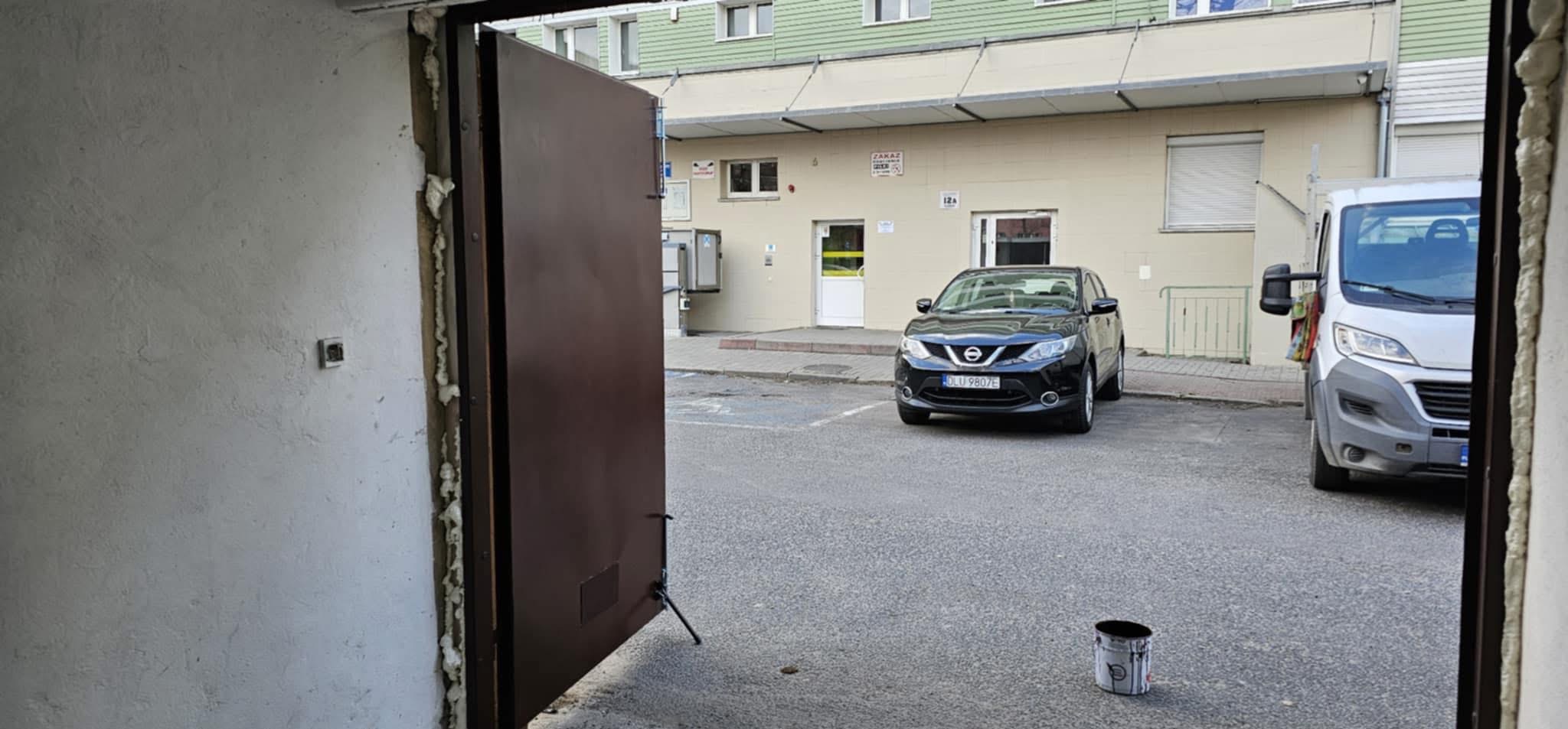 Montaż brązowej bramy garażowej z widoczną pianką montażową. Na zewnątrz zaparkowany samochód i bus.