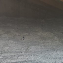 Klaudia Krzyż - Izolacja poddasza pianką poliuretanową, nierównomierna struktura, widoczne fragmenty konstrukcji dachu, szaro-biała kolorystyka, oświetlenie od góry.