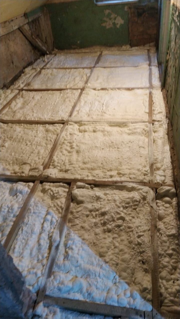 Ocieplenie poddasza pianą PUR, widoczne drewniane elementy konstrukcyjne. Izolacja termiczna w budynku, aplikacja pianki izolacyjnej.