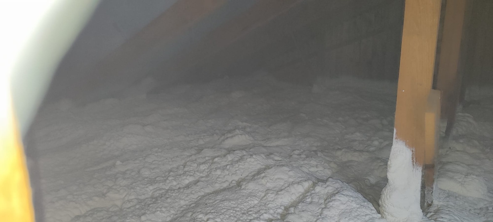 Izolacja poddasza pianką PUR: biała, spieniona warstwa szczelnie wypełnia przestrzeń między drewnianymi elementami konstrukcyjnymi.