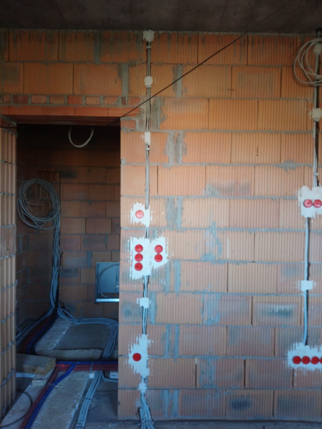 Surowa ściana z cegły z przewodami i puszkami elektrycznymi w trakcie montażu. Widoczne kable w podłodze. Stan surowy budynku.