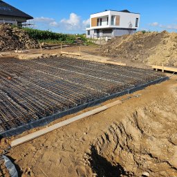 EMEREN SPÓŁKA Z OGRANICZONĄ ODPOWIEDZIALNOŚCIĄ - Zbrojenie fundamentu pod budowę domu jednorodzinnego. Widoczne ułożone pręty zbrojeniowe na czarnej folii, drewniane szalunki i usypana ziemia w tle.