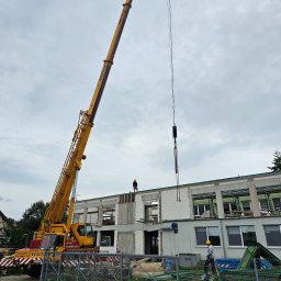 EMEREN SPÓŁKA Z OGRANICZONĄ ODPOWIEDZIALNOŚCIĄ - Budowa budynku z bloczków w Szczecinie. Żuraw podnosi element konstrukcyjny. Pracownicy w kaskach nadzorują proces. Widoczne rusztowania i elementy zabezpieczeń.