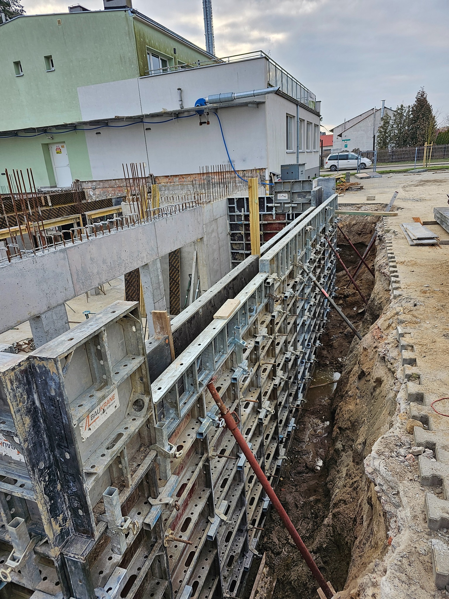 Szczegółowe ujęcie wykopu z szalunkiem systemowym Baukrane, przygotowanego pod fundamenty budynku. Widoczne zbrojenia i elementy konstrukcyjne.