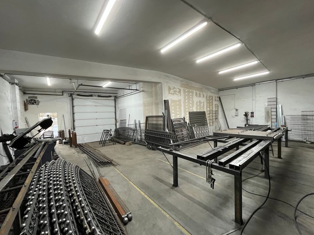 Warsztat spawalniczy z elementami metalowymi do bram i ogrodzeń, w tle brama garażowa i narzędzia do obróbki metalu.