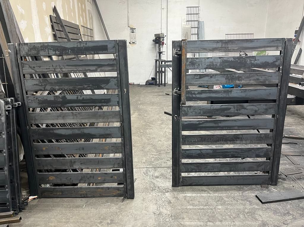 Surowe, metalowe dwuskrzydłowe wrota z poziomymi szczeblami, w trakcie produkcji w warsztacie, widoczne ślady spawania i surowy metal.