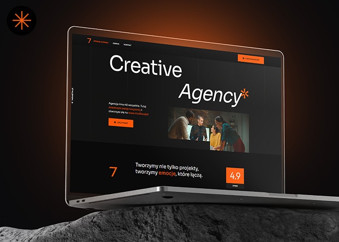 Laptop prezentuje stronę internetową agencji kreatywnej z ciemnym motywem, pomarańczowym akcentem i zdjęciem zespołu. Widoczny fragment skały w tle dodaje unikalności.