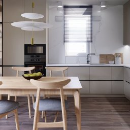 The Plan sp. z o.o. - Nowoczesna, jasna kuchnia z drewnianym stołem i krzesłami. Na stole misa z owocami. Minimalistyczne oświetlenie i zabudowa kuchenna z elementami marmuru.