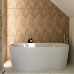 Nowoczesna, biała wanna wolnostojąca na tle ściany z drewnopodobnej mozaiki w łazience w Dobroniu. Złota armatura i marmurowe płytki dodają elegancji.