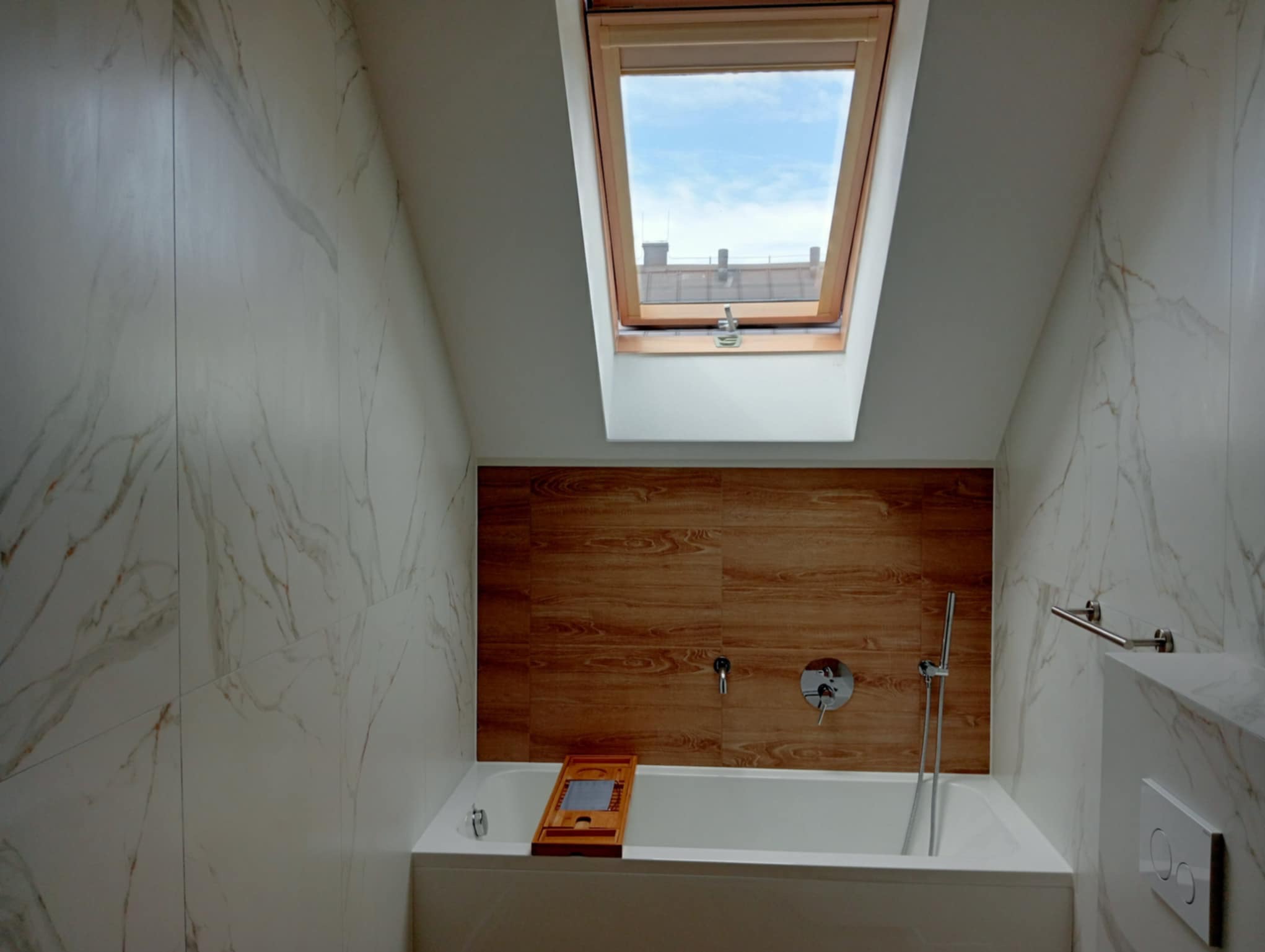 Nowoczesna łazienka na poddaszu z marmurowymi płytkami, drewnianą ścianą, oknem dachowym i białą wanną z drewnianą nakładką. Minimalistyczny design.