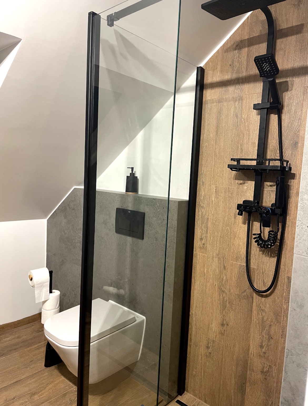 Nowoczesna kabina prysznicowa z czarnymi detalami i drewnopodobnymi płytkami w Zabrzedu. Umywalka podwieszana i minimalistyczna armatura.