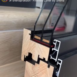 HLO Okna Fenster z polski - Przekrój ramy okiennej z drewna i aluminium, widoczne uszczelki i pakiety szybowe, na jasnej podłodze.