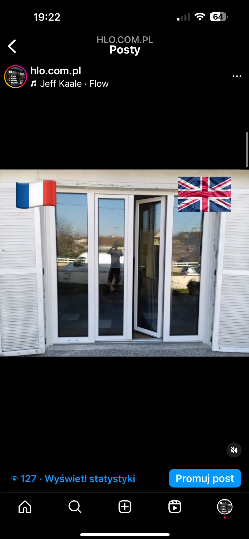 Białe, przeszklone drzwi balkonowe PCV z częściowo otwartym skrzydłem, widoczne odbicie osoby robiącej zdjęcie, z naklejonymi flagami Francji i Wielkiej Brytanii.