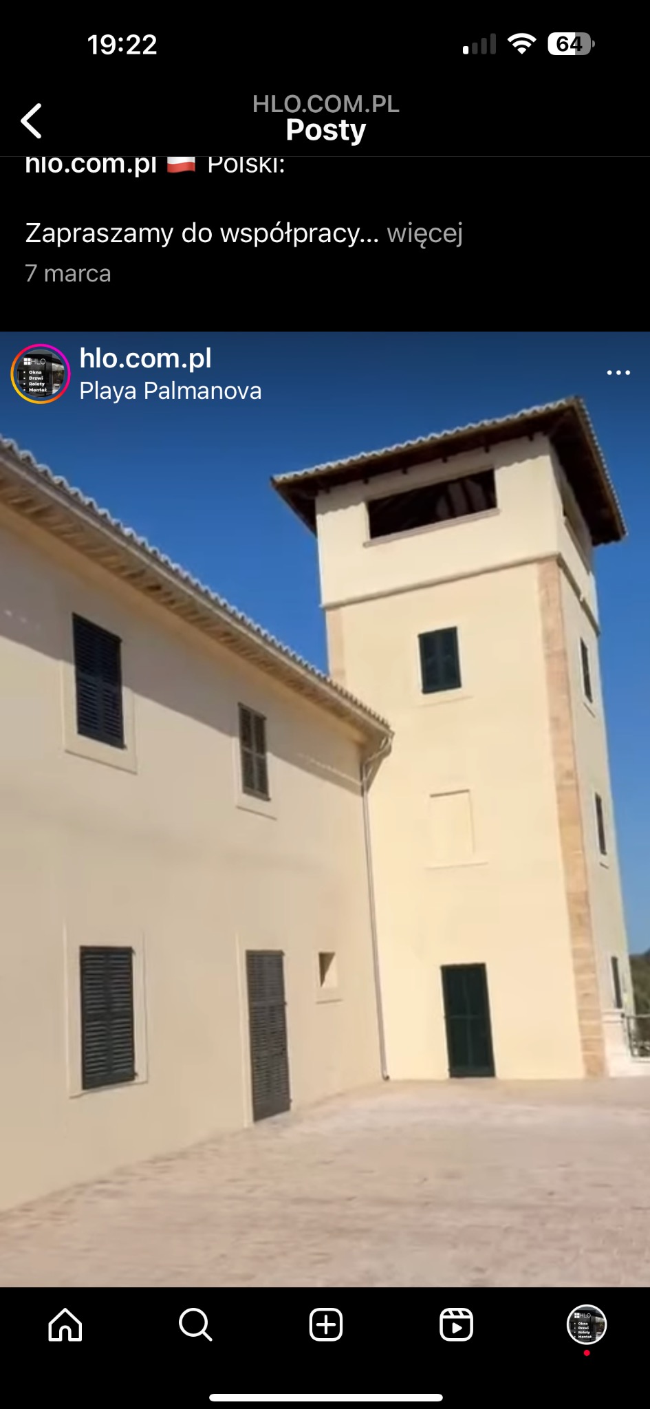 Jasna elewacja budynku z ciemnymi okiennicami i wieżą obserwacyjną pod błękitnym niebem.