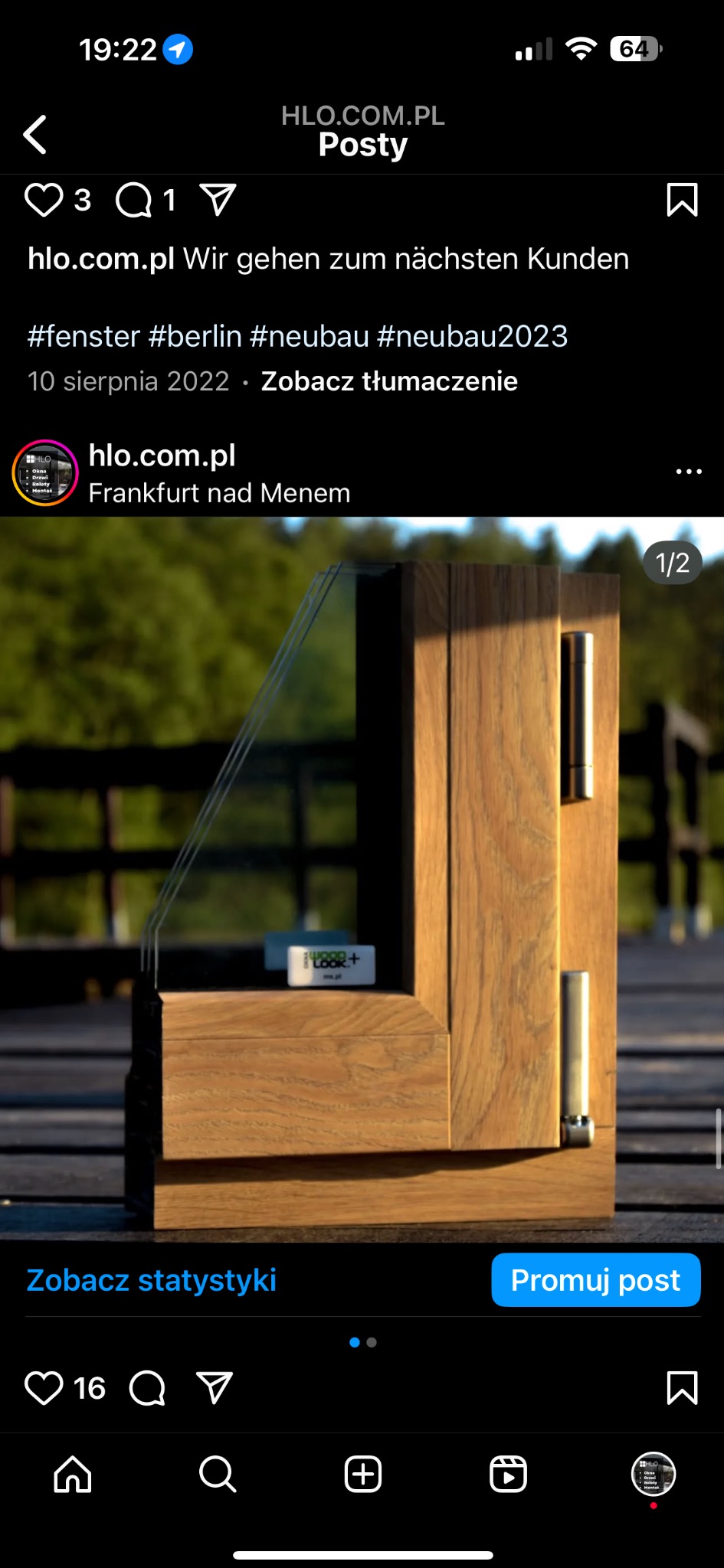 Przekrój drewnianej ramy okiennej z szybą zespoloną, widoczne okucia i etykieta producenta szkła, na tle zieleni.