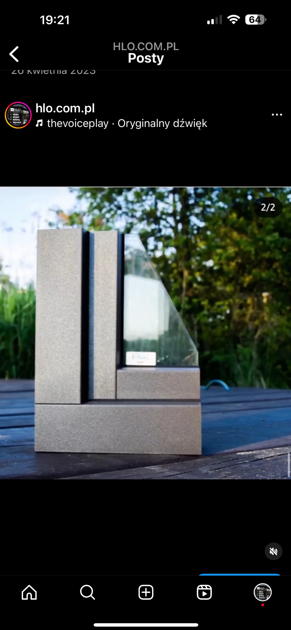 Przekrój okna z szarą ramą, prezentowany na drewnianym stole na tle zieleni.