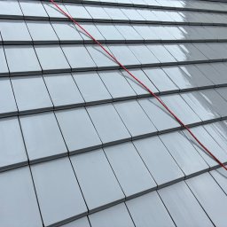 Jarek Wachowiak - Błyszczący, szary dach z dachówki ceramicznej, na którym widoczna jest czerwona lina. Dach świeżo po umyciu, odbija światło, ukazując czystą powierzchnię.