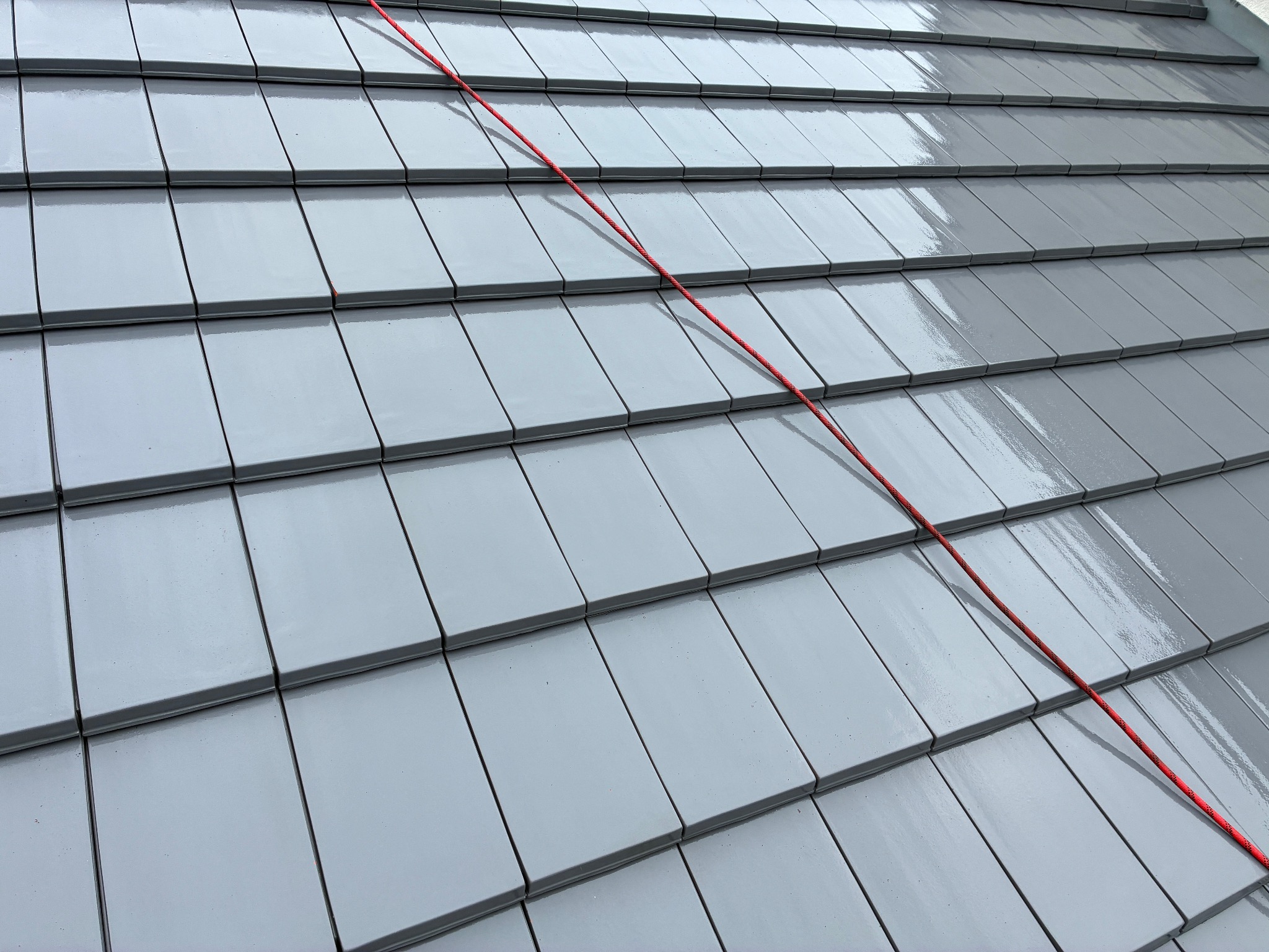 Błyszczący, szary dach z dachówki ceramicznej, na którym widoczna jest czerwona lina. Dach świeżo po umyciu, odbija światło, ukazując czystą powierzchnię.