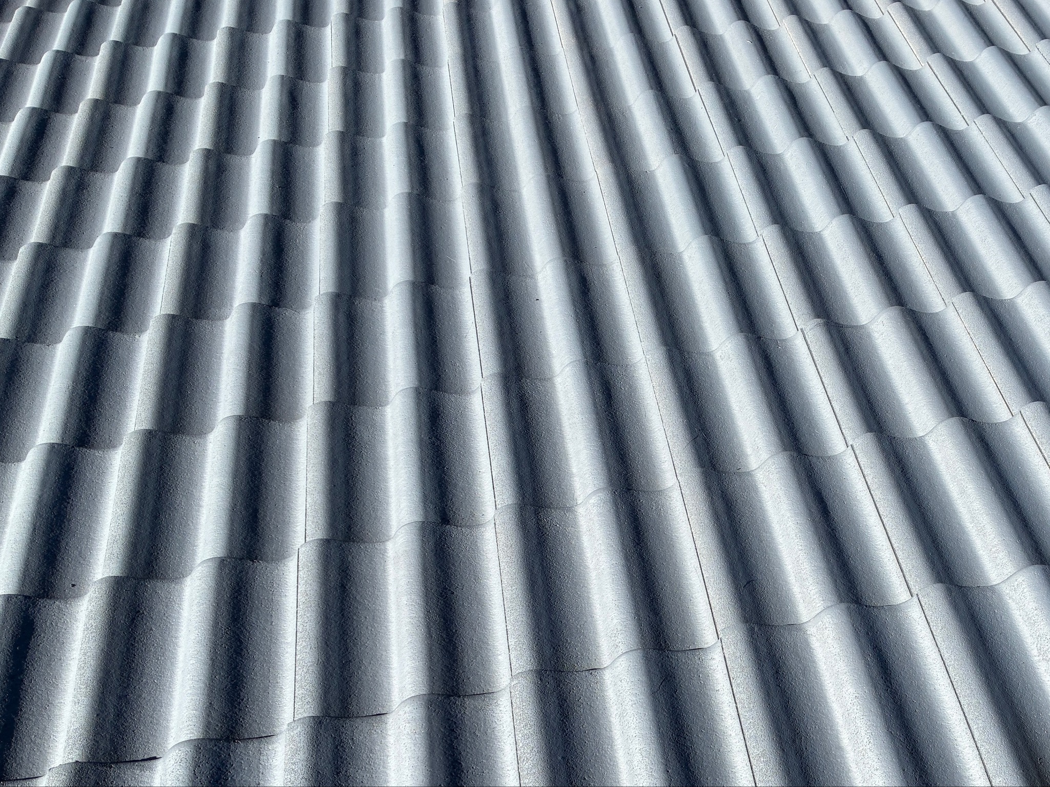 Czysty, szary dach z falistej dachówki ceramicznej, widziany pod kątem. Regularny wzór, mocne cienie podkreślają fakturę. Świeżo umyty dach.