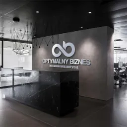 Nowoczesne biuro z recepcją z czarnego marmuru, logo 'Optymalny Biznes' na szarej ścianie, widok na przestrzeń biurową z oknami i stanowiskami pracy. Minimalistyczny design.