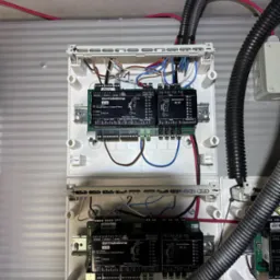 Dwa białe panele sterowania Dormakaba 92.00 i 90 31 z podłączonymi kablami, zamontowane na ścianie. Widoczne przewody w peszlach.