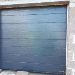 Przedsiębiorstwo Handlowo Usługowe Mariusz Mażul - Zamknięta, segmentowa brama garażowa Hormann w odcieniach szarości, widoczna z bliska na tle surowych, betonowych bloczków ściany garażu.