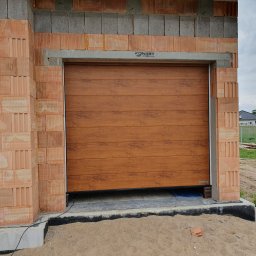 Przedsiębiorstwo Handlowo Usługowe Mariusz Mażul - Zamknięta brama garażowa segmentowa w kolorze drewna, w surowym otworze budynku z cegły. Widoczna marka Konbet Poznań i Hormann. Tło: budynki mieszkalne.