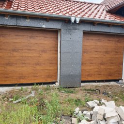 Przedsiębiorstwo Handlowo Usługowe Mariusz Mażul - Dwie brązowe bramy garażowe segmentowe, z widoczną strukturą drewna, zamontowane w surowym otoczeniu, z elementami budowlanymi na ziemi.