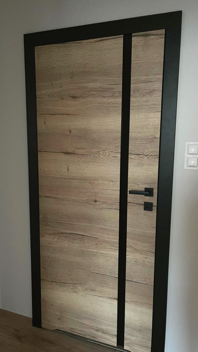 Drewniane drzwi wewnętrzne z czarną ramą i wstawkami, widoczna klamka z zamkiem.