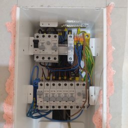 Smart Technik Gliwice - Rozdzielnica elektryczna Eaton w białej obudowie, zabezpieczona pianką montażową, z widocznymi bezpiecznikami i okablowaniem w kolorach niebieskim, brązowym i zielono-żółtym.