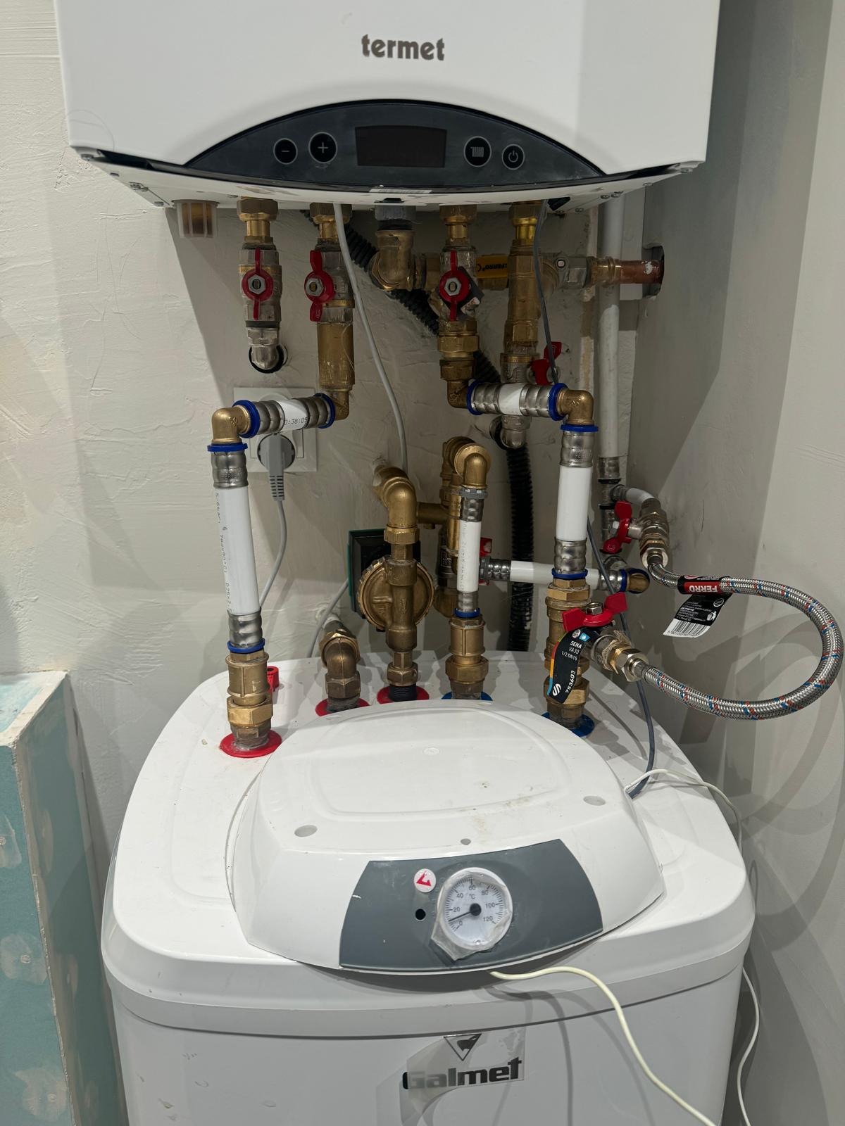 Zamontowany piec gazowy Termet z widocznymi przyłączami, rurami i zaworami. Instalacja wykonana schludnie, z dbałością o detale. Widoczny manometr Galmet.