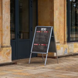 REYDESIGN JAKUB SZYMAŃSKI - Dwustronny, srebrny stojak reklamowy z menu restauracji w Woli Łaszewskiej, ustawiony na chodniku przed wejściem do lokalu z kolumnami w tle.