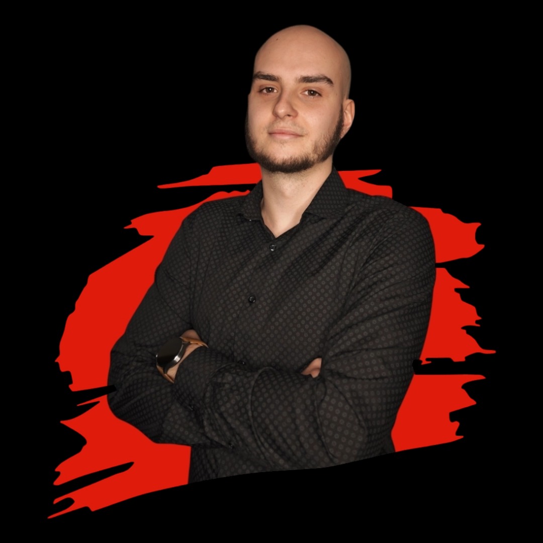 Portret brodatego mężczyzny z założonymi rękami, ubrany w ciemną koszulę na tle czarno-czerwonej abstrakcji.