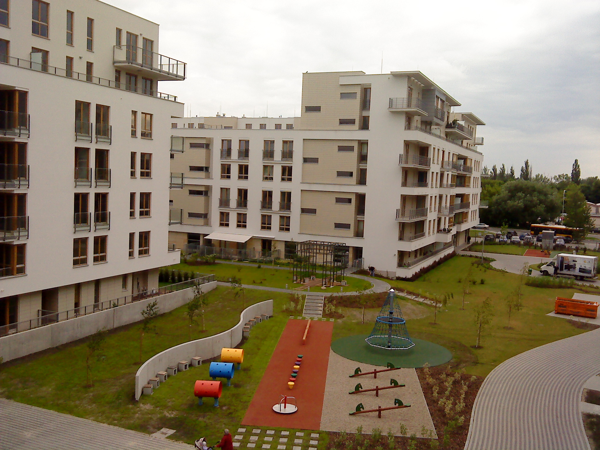 Nowoczesne osiedle apartamentów z placem zabaw w Warszawie, widok z góry na budynki z balkonami i kolorowe elementy wyposażenia dla dzieci.