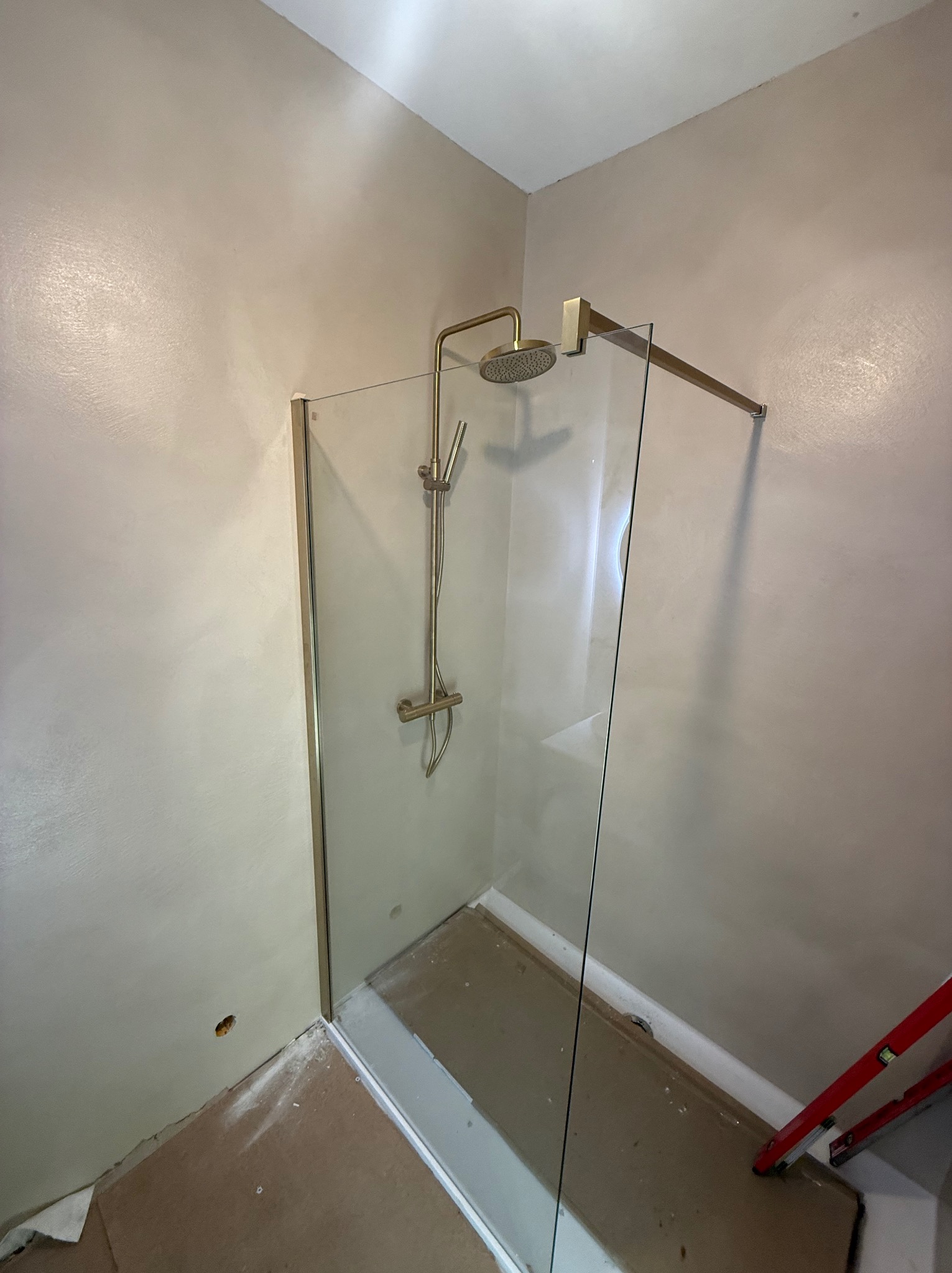 Nowoczesna kabina prysznicowa z złotą armaturą i szklanymi ściankami, widoczna w rogu łazienki w trakcie wykańczania. Na podłodze widoczne ślady prac.