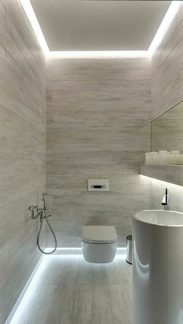 Nowoczesna łazienka z podświetleniem LED: ściany i podłoga wyłożone płytkami imitującymi drewno, wisząca toaleta, wysoka umywalka kolumnowa, bidetka, lustro z półką na świece.