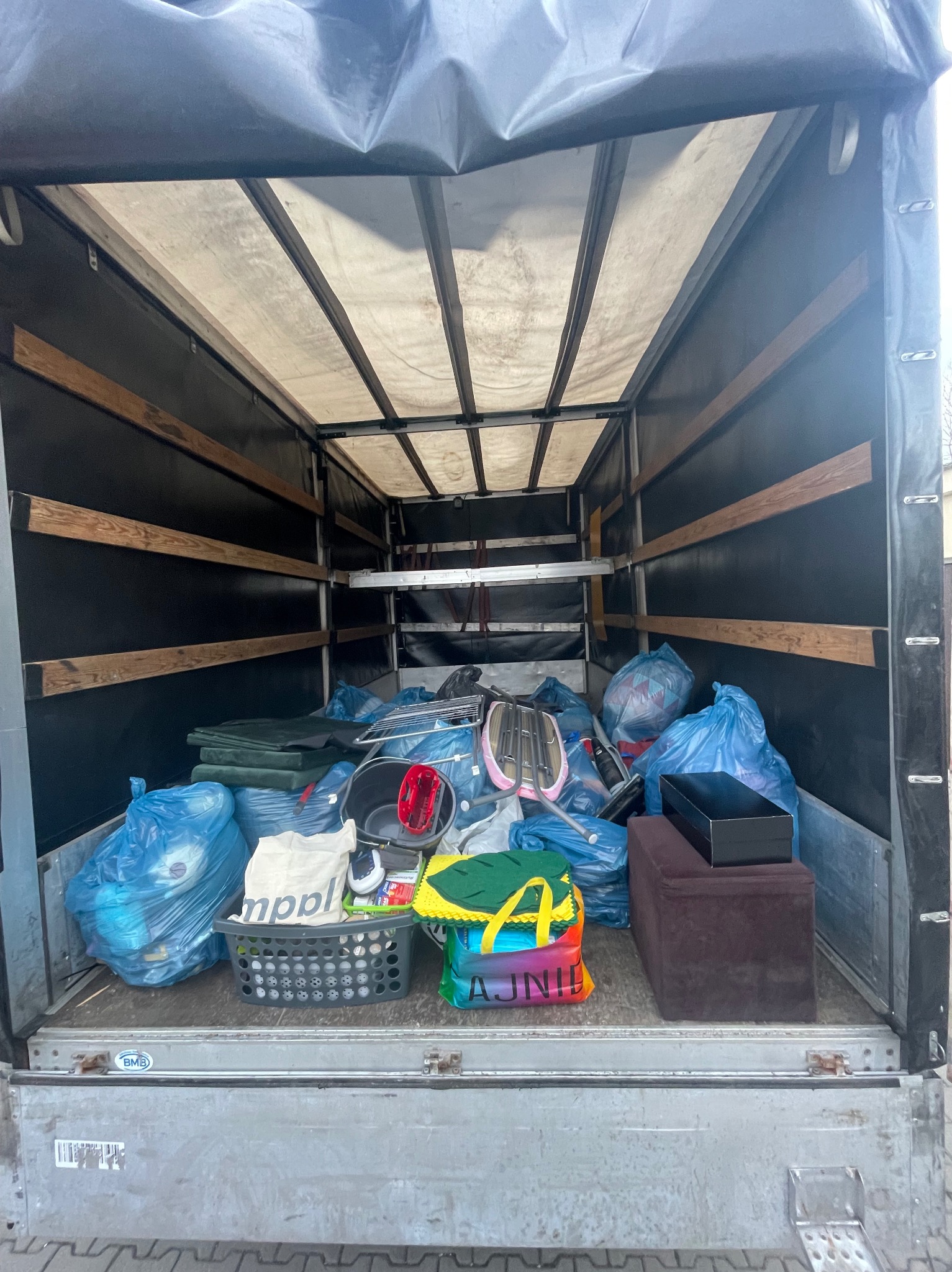 Wnętrze skrzyni ładunkowej wypełnione po brzegi workami i przedmiotami, zabezpieczone czarną plandeką, gotowe do transportu.