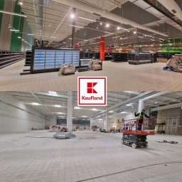 DALF - Rozległe wnętrze sklepu w trakcie wykańczania: regały, instalacje, podnośnik z pracownikiem. Widok na sufit z instalacjami. Logo Kaufland nałożone na zdjęcie.