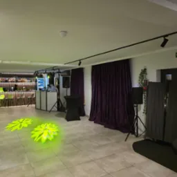 Sala bankietowa przygotowana na imprezę: bar z oświetleniem, stanowisko DJ-a, nagłośnienie i dekoracyjne światła na podłodze.