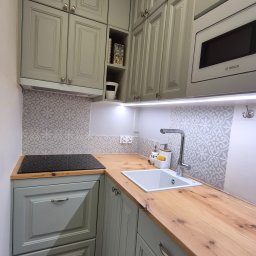 MRS SPÓŁKA Z OGRANICZONĄ ODPOWIEDZIALNOŚCIĄ - Jasnoszara kuchnia na wymiar z drewnianym blatem i wzorzystą mozaiką nad blatem. Widoczna płyta indukcyjna i zlew. Oświetlenie LED podszafkowe.