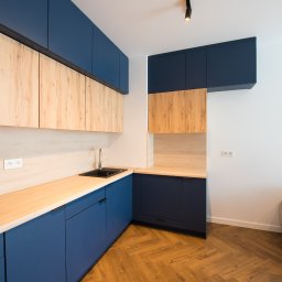 MRS SPÓŁKA Z OGRANICZONĄ ODPOWIEDZIALNOŚCIĄ - Niebiesko-drewniana kuchnia z czarnym zlewem i parkietem w jodełkę. Górne szafki z drewnianymi frontami, dolne i wiszące szafki w kolorze granatowym. Nowoczesny design.