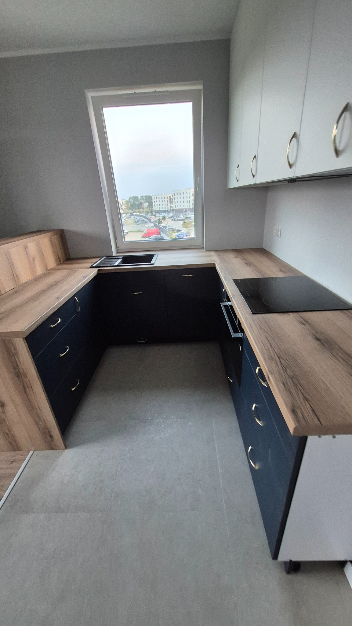 Nowoczesna kuchnia na wymiar z czarnymi frontami i drewnianym blatem, umieszczona pod oknem na poddaszu. Widoczne płyta indukcyjna i zlew.