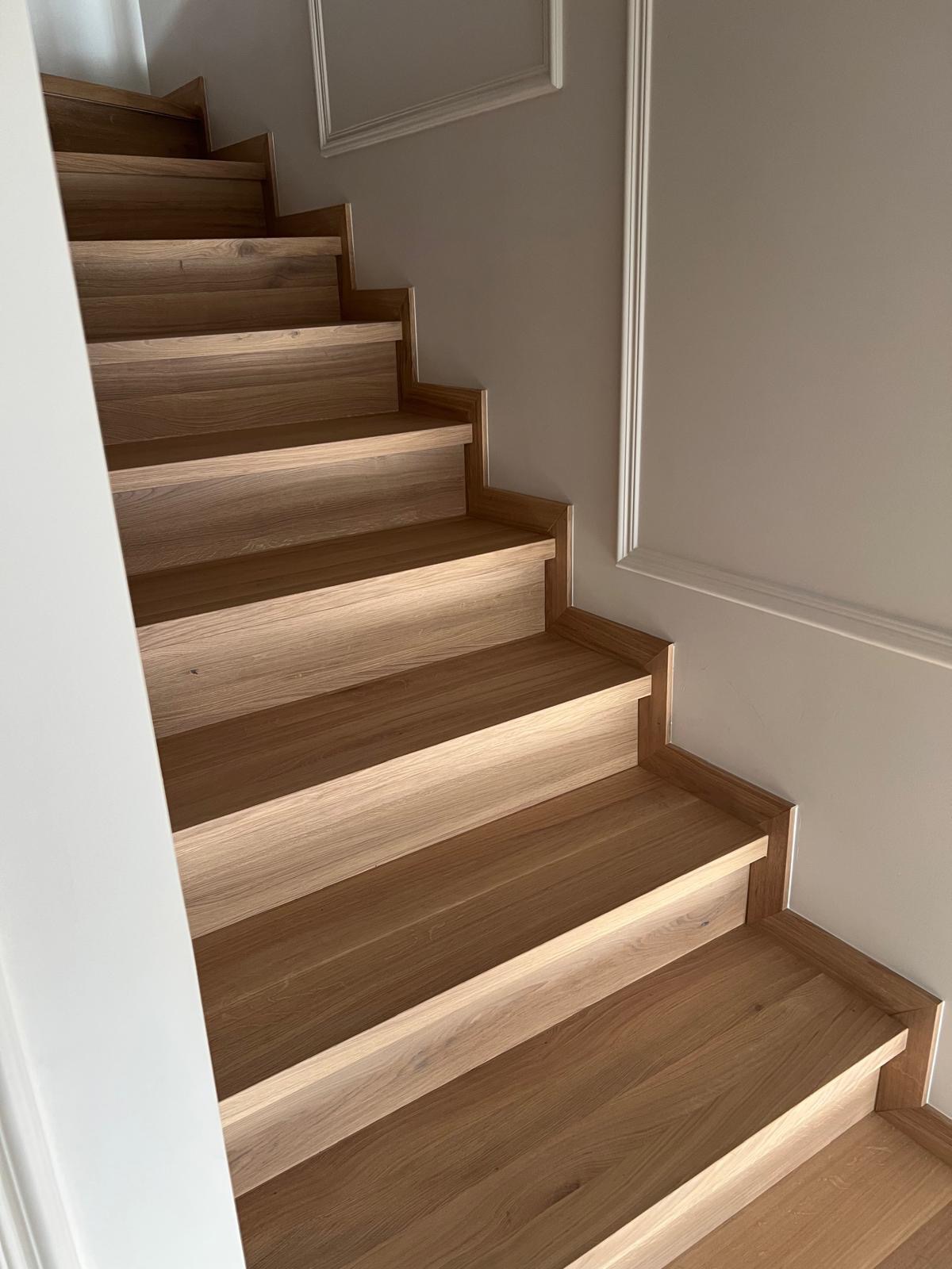 Jasne, dębowe stopnie schodów z minimalistycznym wykończeniem, widok z dołu, dekoracyjna listwa ścienna w tle.