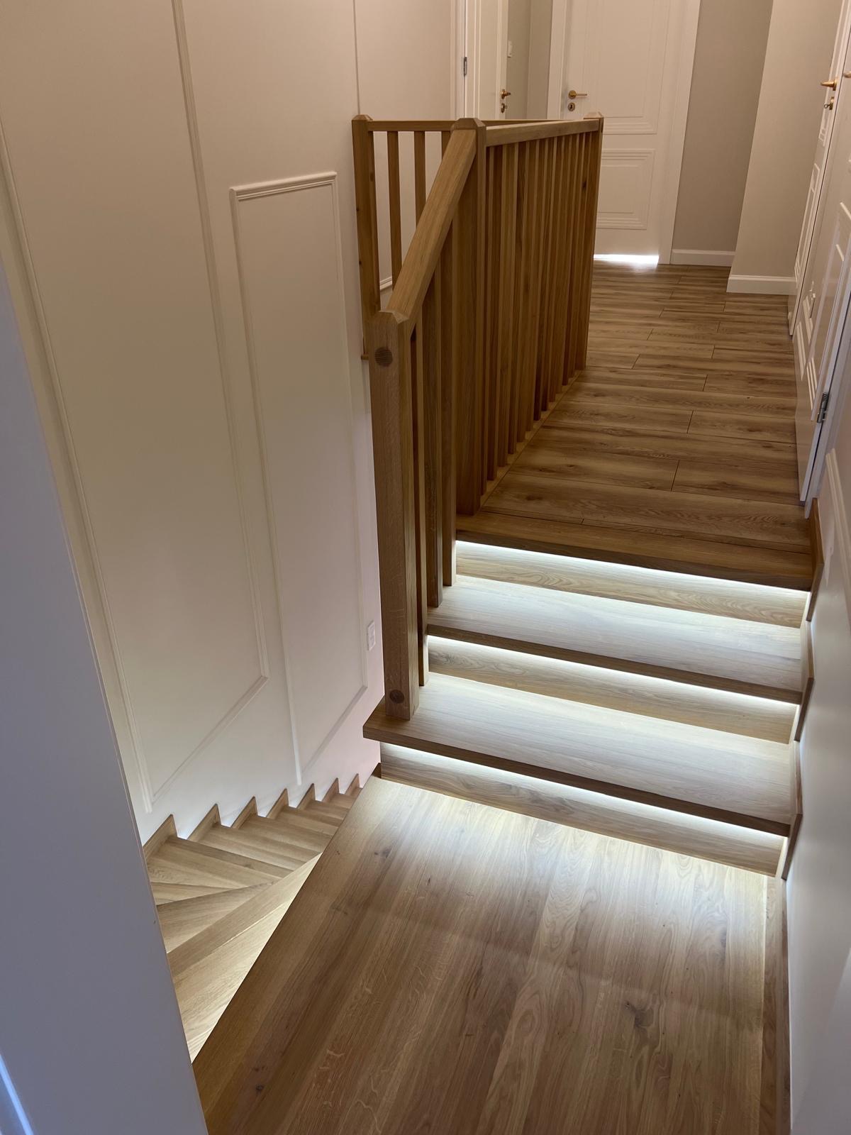 Nowoczesne schody z drewna z podświetleniem LED na każdym stopniu i drewnianą balustradą, widok z góry.