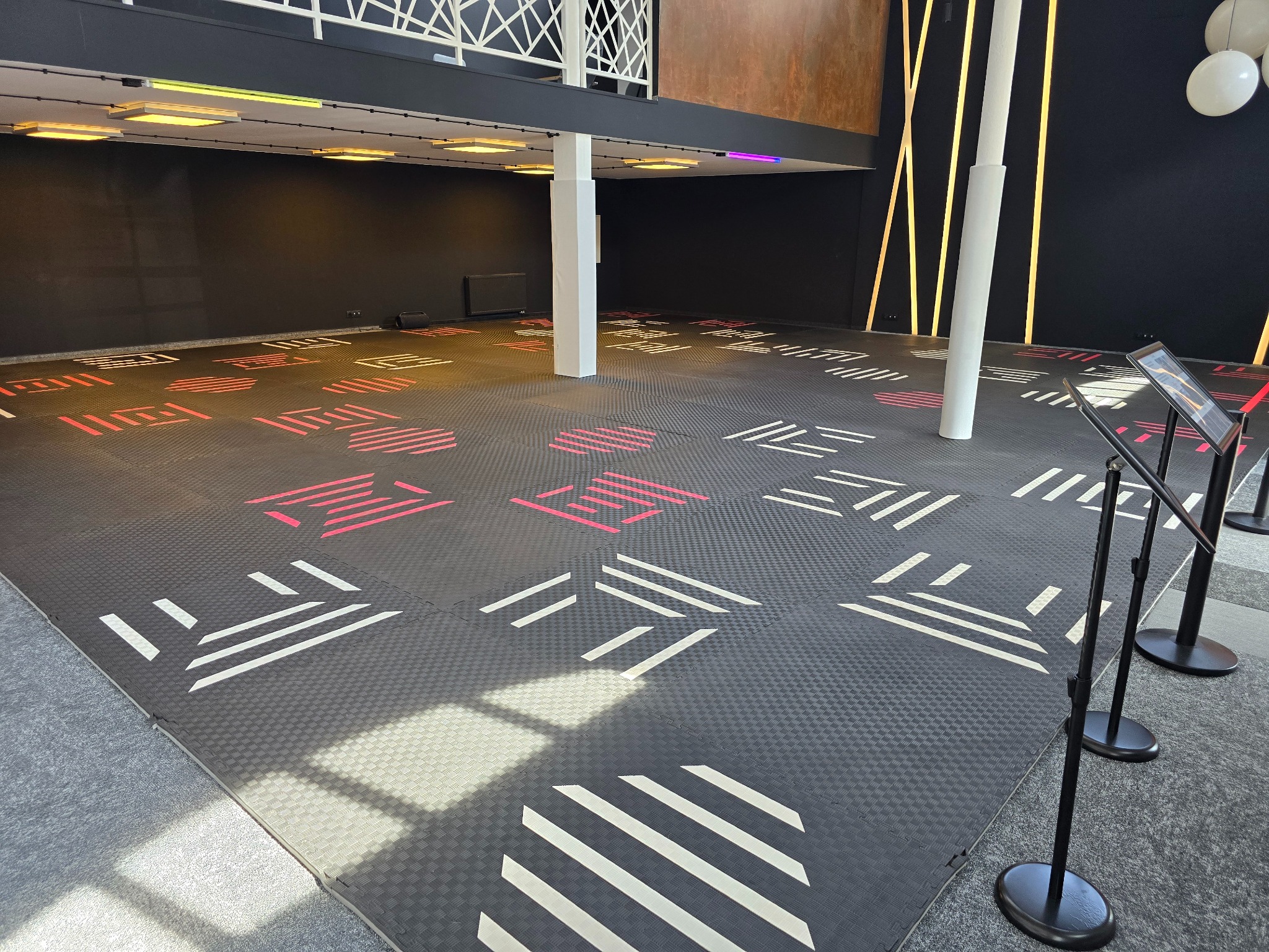 Pusta sala eventowa z czarną podłogą w geometryczne wzory, białe kolumny i oświetlenie sufitowe.